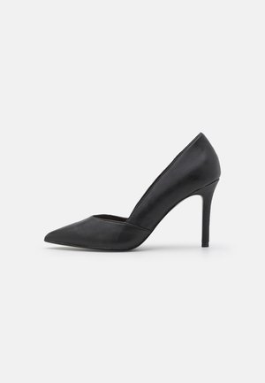 Chaussure à talon haut en cuir noir à bout pointu avec un talon stiletto fin sur un fond clair uni.