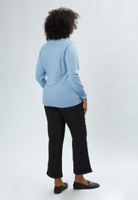 Maglione azzurro chiaro con maniche lunghe e orlo a coste, abbinato a pantaloni neri con risvoltini e scarpe basse nere.
