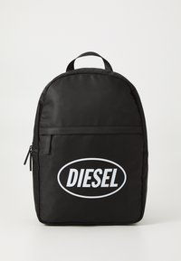 Juodas nailono kuprinės forma su apvaliais kraštais, ant priekinės pusės didelis baltas "DIESEL" logotipas, viršuje esantis rankenėlis ir priekinė kišenė su užtrauktuku.