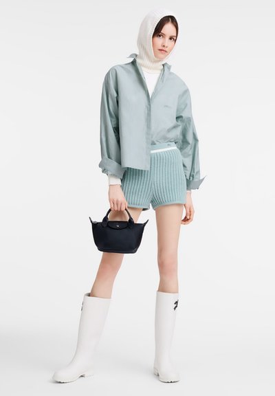 Hellblaue übergroße Bluse, weißer gerippter Rollkragenpullover, strukturierte mintfarbene Shorts, schwarze Handtasche und glänzende weiße kniehohe Stiefel.