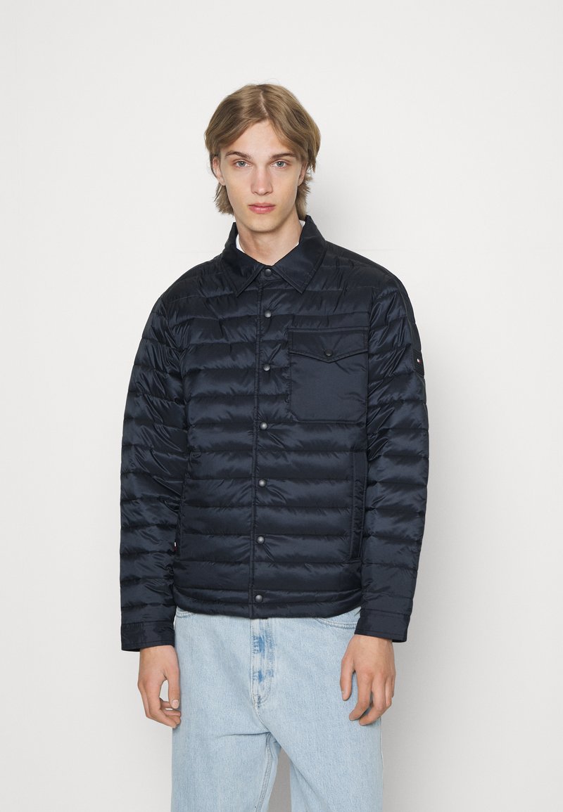 Giacca puffer blu navy con chiusura a bottoni, texture trapuntata, taschino sul petto e branding discreto sulla manica.