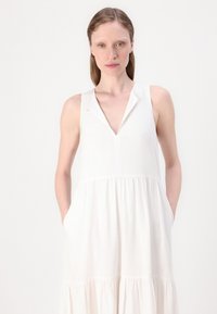 Bala bezrokas kleita ar V-veida kaklu un apkakli, ar pakāpenisku dizainu, maigu tekstūru un sānu kabatām. Vienkārša un eleganta forma.