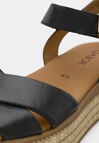 Μαύρο δερμάτινο σανδάλι με δύο φαρδιές λουράκια, σόλα από τζούτ σε στυλ εσπαντρίγια και καφέ πάτο. Διαθέτει πόρπη στο λουράκι του αστραγάλου.