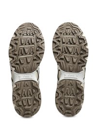 Athletic shoe soles featuring a textured tread pattern in beige and black, with a white midsole and branding detail on the side.