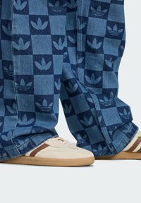 Blue checked denim pants with darker blue leaf patterns, paired with beige sneakers featuring brown accents and a textured sole.