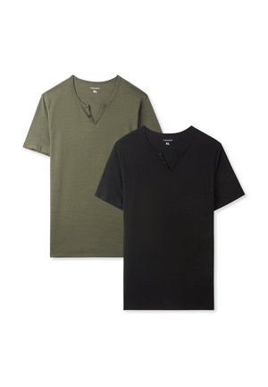 Maglietta henley a maniche corte color verde oliva, dal tessuto morbido, abbinata a jeans a gamba dritta blu chiaro e sneakers bianche. Sfondo neutro.