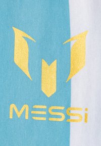 Tecido azul claro e branco com um grande logotipo dourado apresentando elementos estilizados e o texto "MESSI" numa fonte negrito e moderna.