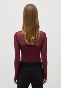 Body de manga larga burdeos con sección superior transparente, combinado con jeans negros de tiro alto. Textura suave, diseño ajustado.