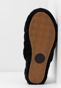 Black fuzzy slipper with a rubber sole featuring a sunburst pattern and a circular logo. Soft texture with a rounded shape.