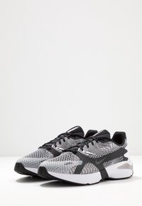 Scarpe sportive bianche e nere con tomaia in rete, pattern geometrici a contrasto e una spessa suola bianca per ammortizzazione e supporto.