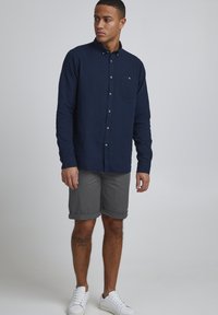 Navy button-up long-sleeve shirt with a chest pocket; gray rolled shorts; white sneakers; smooth fabric; relaxed fit.