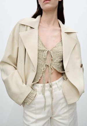 Beige oversized blazer över en ljusgrön texturerad crop top med framslipsdetalj, tillsammans med högmidjade vita byxor.