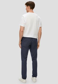 Herren T-Shirt aus weißer Baumwolle, kurze Ärmel, kombiniert mit navy gestreiften Hosen und weißen Sneakern; sichtbare Nähte und Details am Bund.