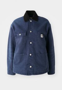 Giacca button-up blu navy con colletto in velluto a coste nero, quattro tasche frontali e bottoni a pressione in metallo, con un piccolo logo sulla tasca del petto.