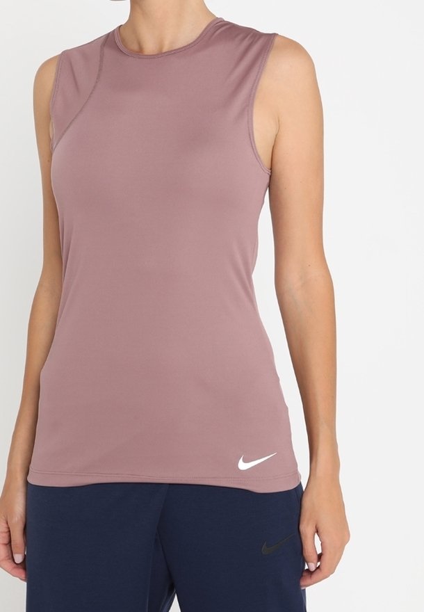 Haut de sport sans manches mauve avec logo Nike blanc porté par une personne debout sur fond blanc, associé à un pantalon Nike bleu marine.