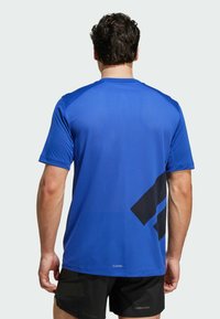 Camiseta deportiva azul con textura de malla, mangas cortas y un gran acento gráfico negro en la parte posterior. Hecha de un material transpirable.