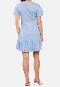 Vaaleansininen mekko, jossa on lyhyet puffihihat, käyristetty yläosa ja levenevä hame, jossa on brodeerattua reikäkoristetta helman varrella.