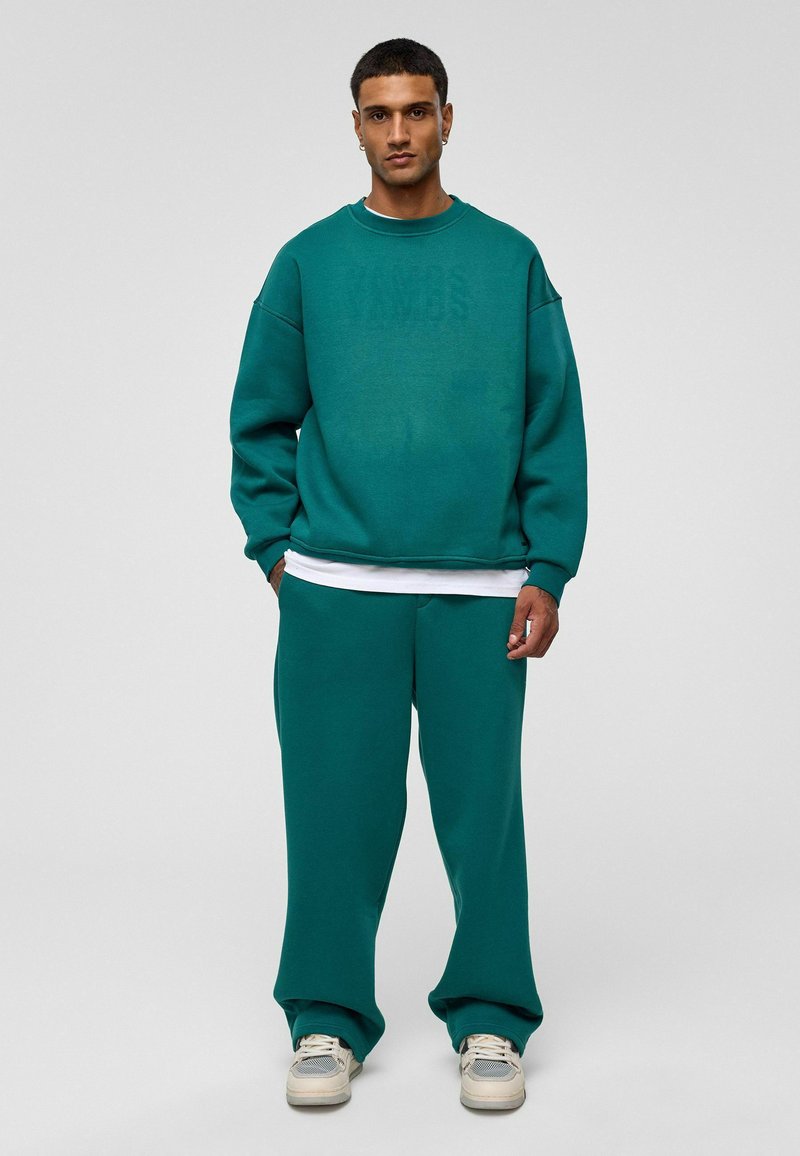 Teal sweatshirt met een losse pasvorm, geribde manchetten en een ronde hals, gecombineerd met bijpassende sweatpants. Heeft een gelaagd wit shirt eronder.
