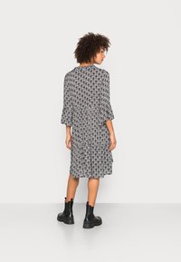 Robe à motifs noir et blanc avec des manches cloche trois-quarts, longueur genoux, en tissu léger, associée à des bottes noires imposantes.