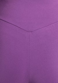 Lila kroppsnära plagg med en slät textur. Har en chevronsömsdesign i mitten som skapar en subtil visuell accent.