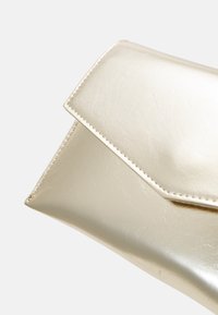 Metallic gold clutch with a smooth, shiny surface, featuring a diagonal flap closure and white stitching along the edge.