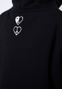 Black hoodie featuring white graphic accents, including two heart designs: one with a yin-yang symbol and another with a peace sign.