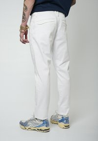 Pantalones blancos de corte ajustado con una textura suave, que cuentan con bolsillos traseros, combinados con zapatillas deportivas grises y azules. Diseño sencillo, color versátil.