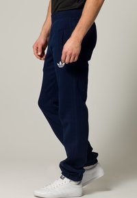 Mörkblå sportbyxor i mjukt tyg, med vita tre-randiga detaljer och logotyp, elastiska muddar och sidofickor.