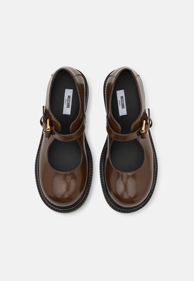 Zapatos Mary Jane de charol marrón con punta redonda, correa ajustable y hebilla dorada, que cuentan con una suela negra texturizada.