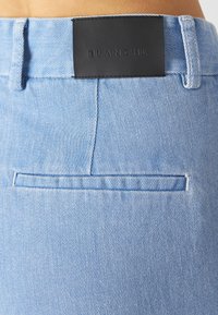 Light blue denim jeans feature a smooth texture, a back pocket, and a black leather label with "BLANCHE" embossed at the waistband.