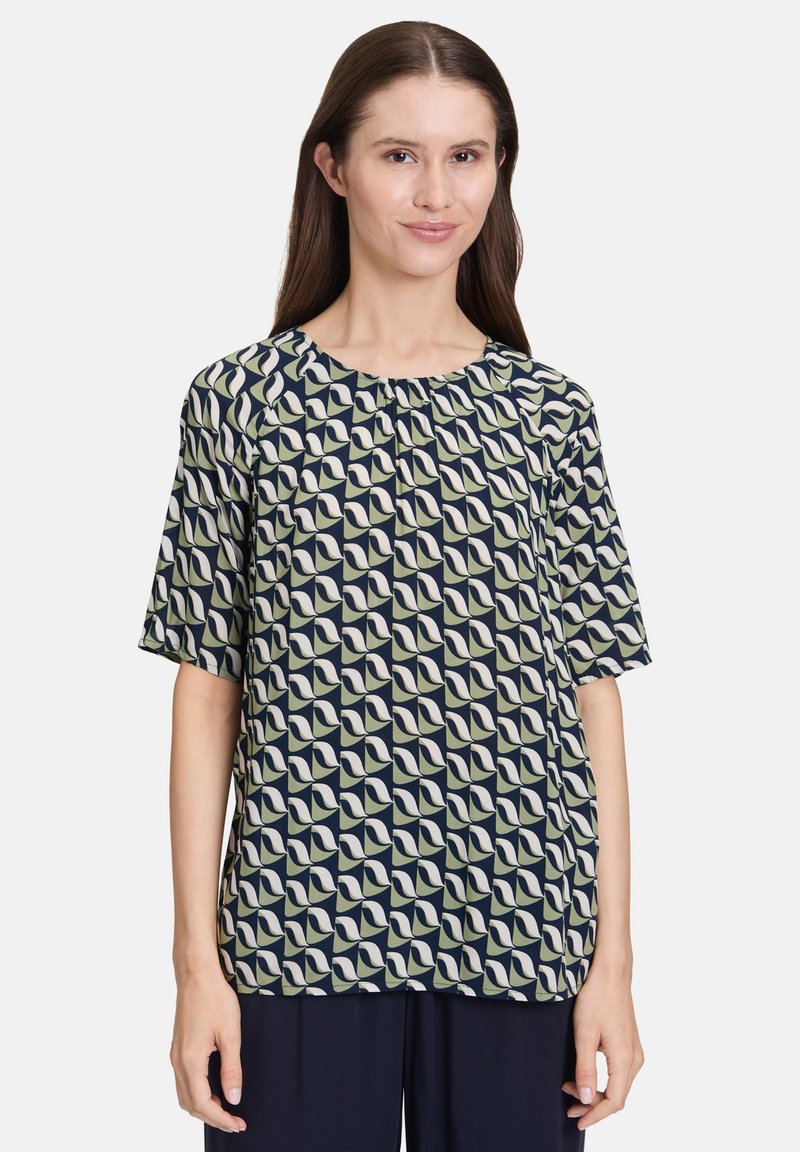 Koszulka krótki rękaw w kolorze granatowym i jasnym zielonym, z geometrycznym wzorem z abstrakcyjnymi kształtami. Miękka tkanina, okrągły dekolt, luźny krój.