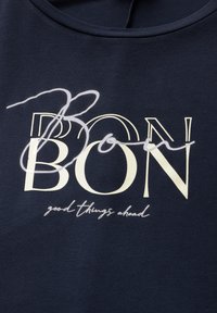 Sweat-shirt bleu marine arborant un graphisme prominent en crème, avec le mot "BON" accompagné d'une touche cursive, et le texte "de bonnes choses à venir" en dessous.