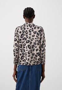Blouse à imprimé léopard beige et noir, manches longues, coupe décontractée, avec un col rond et un tissu doux. Associée à une jupe en denim bleu.