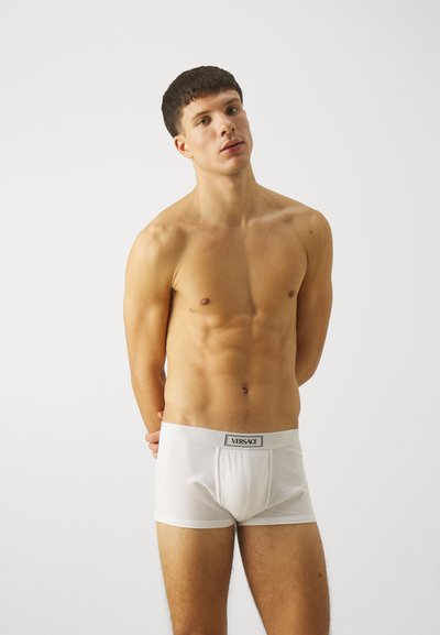 Witte katoenen boxershorts met een elastische tailleband met het zwarte "VERSACE" logo. De stof lijkt zacht en glad.