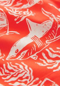 Tissu rouge avec un motif de requin blanc et de corail. La texture semble lisse et brillante, mettant en valeur le design graphique audacieux.