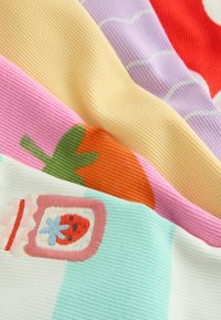 Gros plan sur un tissu côtelé avec des motifs colorés de fruits et de bocaux, dont une fraise, une orange et un bocal avec une étiquette fraise.