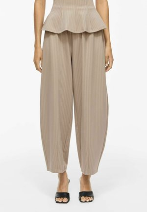 Pantalon beige à larges jambes rayé, porté avec un haut assorti et des sandales mules noires à bout ouvert, montré sur une personne debout.