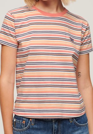 Persoon die een gestreept T-shirt met korte mouwen draagt in perzik, crème en marine met een klein logo op de linkerborst en een kersentatoeage op de onderarm.