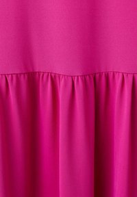 Tissu rose vif avec une couture horizontale créant des plis froncés sous la couture, montrant la texture et le drapé du matériau.