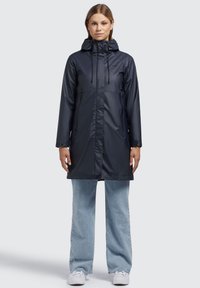 Parka impermeable de color azul marino con capucha, que presenta un cierre frontal, dos bolsillos laterales y cordones ajustables. Textura suave y brillante.