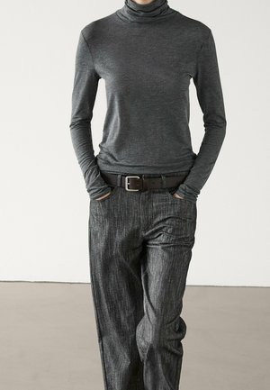 Personne portant un col roulé gris foncé ajusté et un pantalon texturé gris foncé ample, les mains dans les poches et une ceinture noire.
