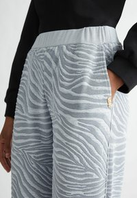 Grå mønstrede joggers med et struktureret zebra-stribedesign, elastisk talje og sidelommer, med en guld accentsdetail.