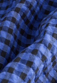 Tissu à carreaux bleu et noir avec un tissage texturé présentant des carrés alternés selon un motif régulier. Fini doux et légèrement brillant.