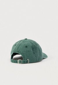 Πράσινο βαμβακερό καπέλο μπέιζμπολ με κυρτή γείσο, ρυθμιζόμενο λουράκι και υφασμάτινη υφή. Η πίσω πλευρά είναι ανοιχτή με ασημί αγκράφα.