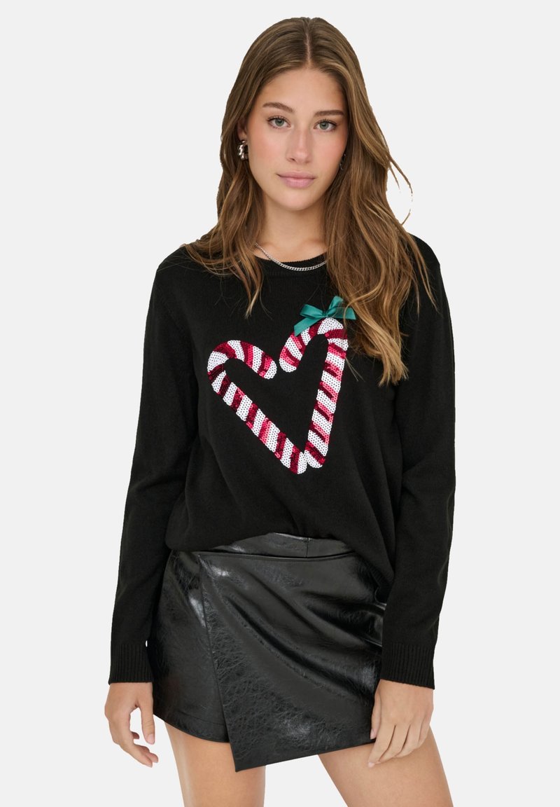 Schwarzer Pullover mit einem rot-weißen gestreiften Herzdesign und einer grünen Schleife. Kombiniert mit einem schwarzen, faux-ledernen Wickelrock.