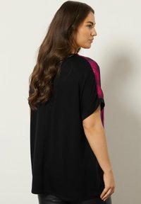 T-shirt nera con maniche corte, con un pannello in gradiente da rosa a viola su ciascun spalla; vestibilità rilassata e texture morbida.