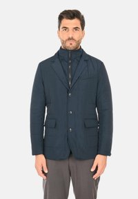 Blazer imbottito blu navy con colletto alto, bottoni frontali, due tasche e design strutturato. Il tessuto ha una finitura liscia e testurizzata.