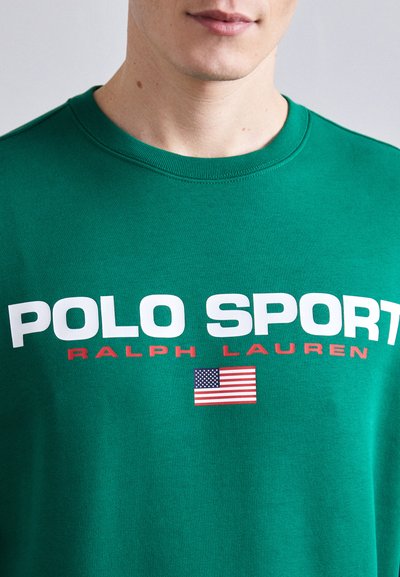 T-shirt en coton vert arborant un grand texte « POLO SPORT » blanc, un accent rouge et un petit graphique du drapeau américain sur le devant. Col rond.