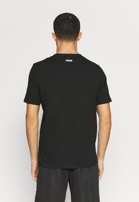 Sort bomulds t-shirt med korte ærmer og rund hals, med et hvidt Puma-logo på ryggen. Enkelt, klassisk design.