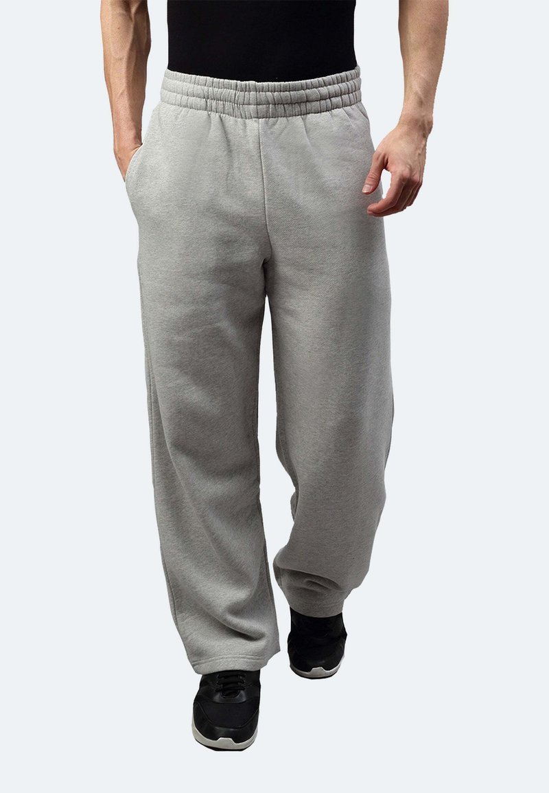 Graue Jogginghosen mit einem elastischen Bund, seitlichen Taschen, lockerer Passform und weichem Material, kombiniert mit schwarzen Sportschuhen.